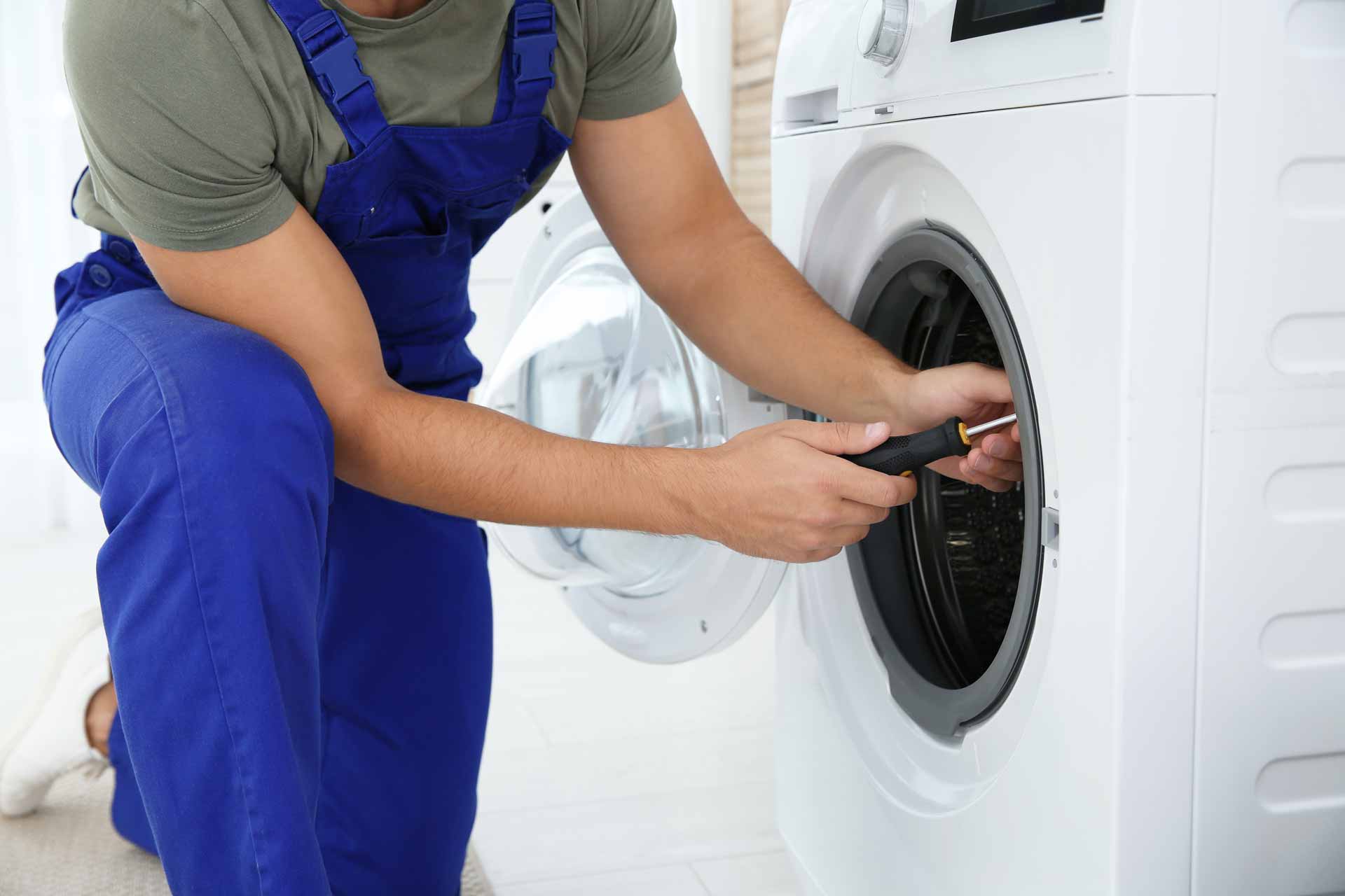Technician in blue overalls repairs a washing machine
